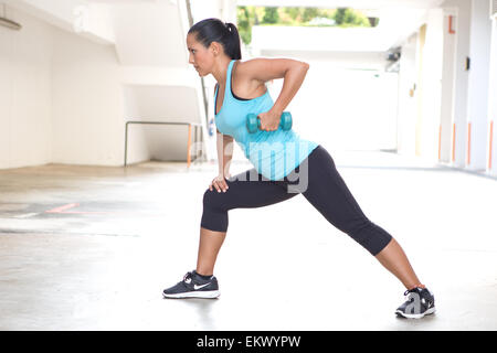 Beautiful sporty hispanic woman in blue  demostrating the rowing routine with blue dumbbell outdoors Stock Photo