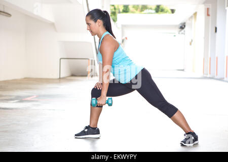 Beautiful sporty hispanic woman in blue  demostrating the rowing routine with blue dumbbell outdoors Stock Photo