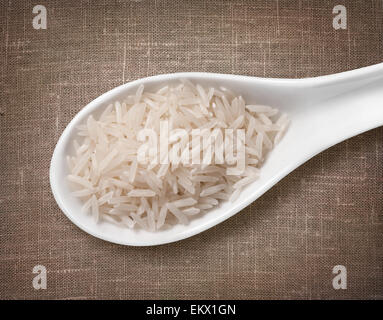 Basmati rice in white porcelain spoon / high-res photo of grain in white porcelain spoon on burlap sackcloth background Stock Photo