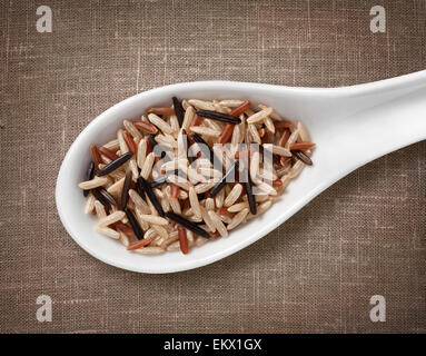 Assorted rice mix in white porcelain spoon / high-res photo of grain in white porcelain spoon on burlap sackcloth background Stock Photo