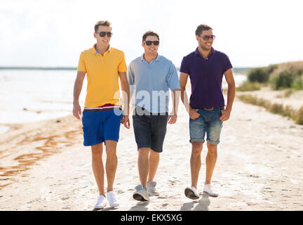 smiling friends in sunglasses walking along beach Stock Photo