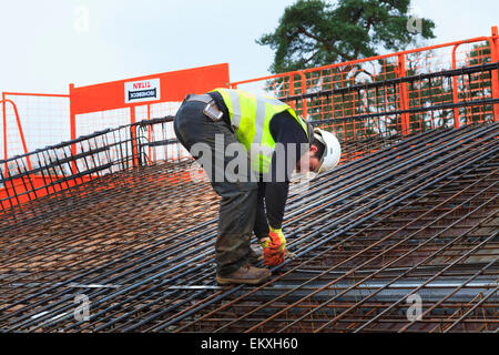 Construction worker tying up reinforcing bars prior to pouring of concrete on a commercial building roof. Stock Photo