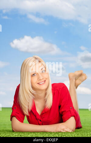 Vertical shot of a blond woman lying on a green grass field outdoors and looking at the camera Stock Photo