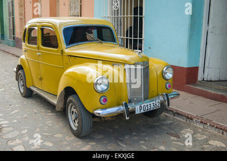 Cuba Trinidad classic vintage old car Ford Prefect 4 door saloon painted gold yellow circa 1951 parked cobbled street Stock Photo