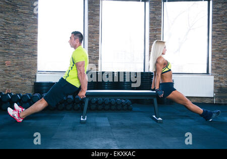 Woman and man doing exercises on hands with bench at gym Stock Photo