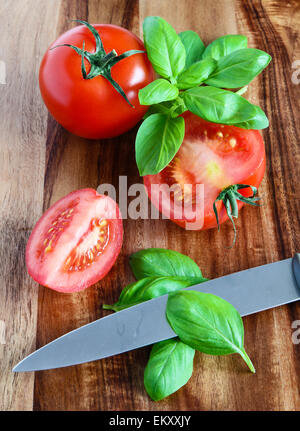 Fresh tomatoes, basil and knife on wooden cutting board Stock Photo