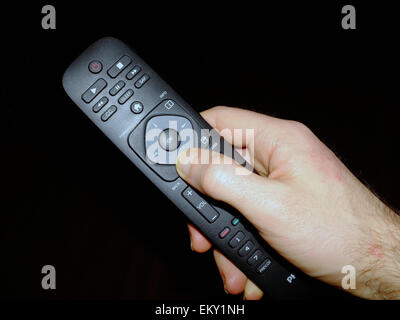 A white hand holding a television controller dice against a black background. Stock Photo