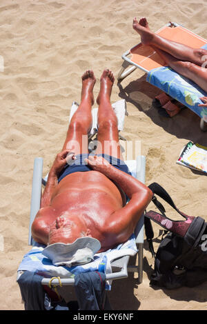 Elderly couple with deep tans sunbathing on beach in Spain Stock Photo