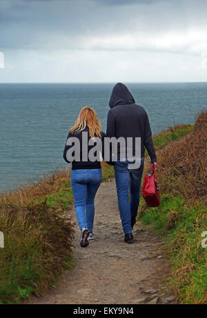 Foreign Polish Migrant couple walk hand in hand on the cliff walk around Howth Head in changeable weather on the coast in North Dublin Ireland Stock Photo