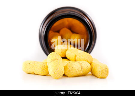 Yellow pills fallen out of brown bottle. Studio shot on white background, view inside bottle. Stock Photo