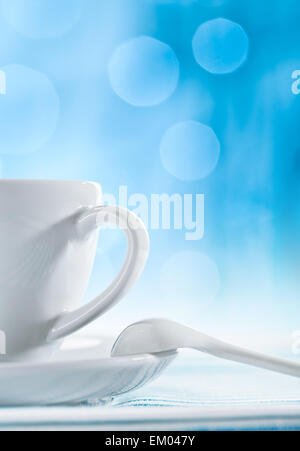 white ceramic cup with spoon on blurry blue background Stock Photo
