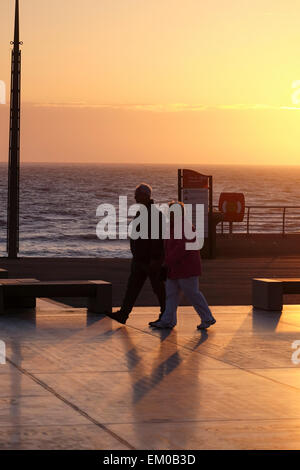 Blackpool, UK: Couple walking along the promenade as the sun sets at the holiday resort of Blackpool on the Fylde Coast Stock Photo