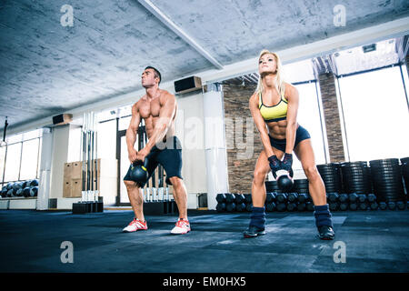 Muscular man and fit woman lifting kettle ball at gym Stock Photo