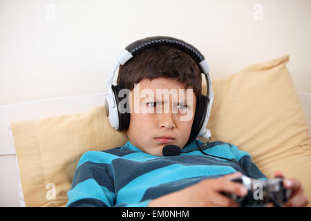 Young boy frowns while playing video game with his friends with headset and microphone with copy space Stock Photo