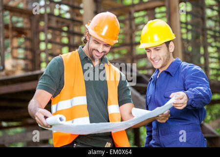 Smiling Architects Analyzing Blueprint At Site Stock Photo