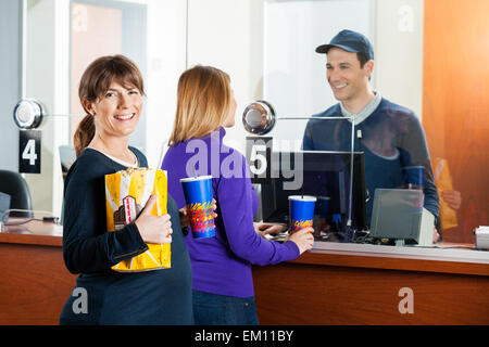 Woman Holding Snacks While Friend Buying Tickets At Box Office Stock Photo