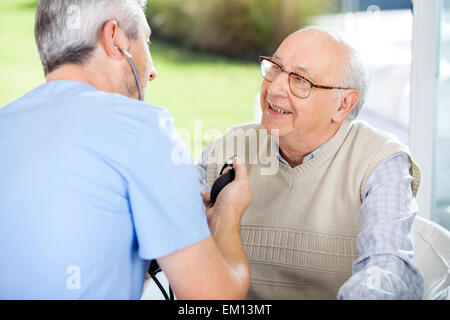 Male Doctor Measuring Blood Pressure Of Senior Man Stock Photo