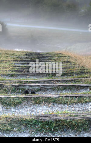 Stairs made of natural wooden planks leads into the morning fog. Stock Photo