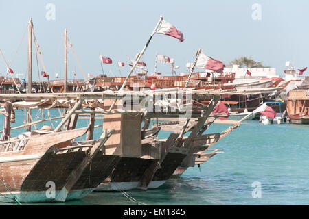 Traditional wooden dhow boats topped by Qatar flags and moored at a dhow wharf in the city of Doha, Qatar. Stock Photo