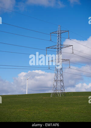 Electricity pylons and a wind turbine crossing a rural grass field in Scotland. Stock Photo