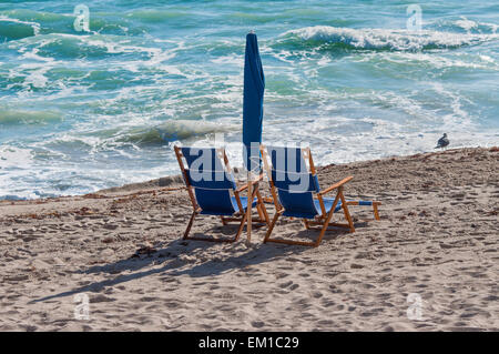 Pair of sun loungers and a folded beach umbrella on a deserted beach Stock Photo