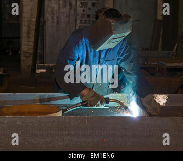Working man with helmet shield on his head is welding  steel construction. Hard work in the production department. Stock Photo