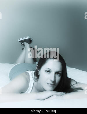Woman lying on her stomach on a bed.  Her feed are up and crossed.  The image has a green and white overtone. Stock Photo