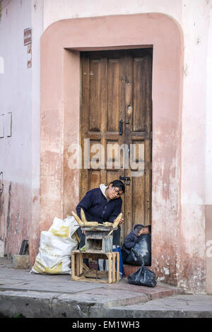 indigenous Mexican Indian woman grills corn street food on sidewalk as her small son naps in doorway San Cristobal de las Casas Stock Photo