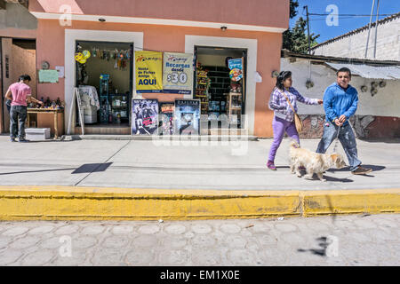 Mexican couple walking fluffy dog on sidewalk try to converse as man struggles with leash to restrain animal San Cristobal Stock Photo