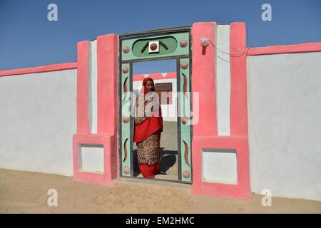 Nubian woman in typical bright dress, in front of her house, in the village of Umogaal in Dongola, Nile Valley, Nubia, Sudan Stock Photo