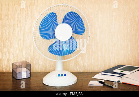 On the table is a handy fan with switching speeds , books, writing materials. Stock Photo