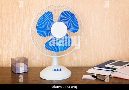 On the table is a handy fan with switching speeds , books, writing materials. Stock Photo