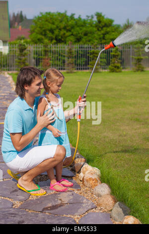 Little cute girl and father watering flowers with hose in their garden Stock Photo