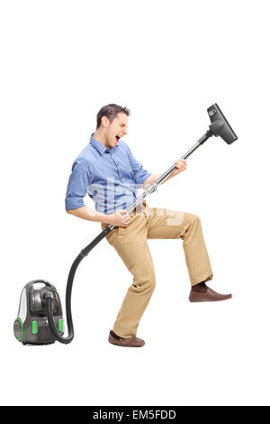 Full length portrait of a silly young man imagining that he plays guitar on a vacuum cleaner isolated on white background Stock Photo