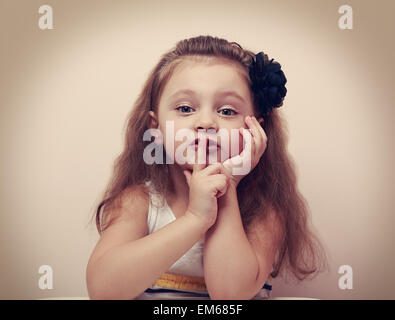 Cute kid girl showing silence sign the finger near lips. Vintage closeup portrait Stock Photo