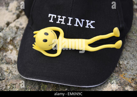 Yellow Smiley Man on holiday in the Outer Hebrides - Here he's lying comfortably on a black baseball cap with the word Think Stock Photo