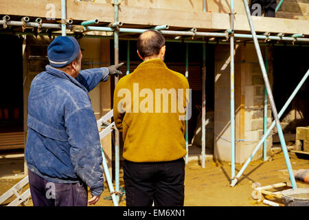 Construction workers discussing work on a building site with scaffolding poles Stock Photo