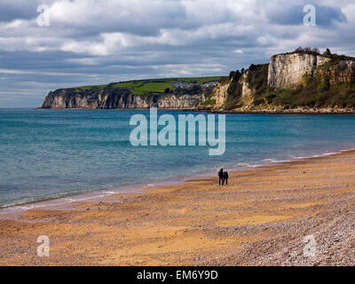 Photograph of a couple walking along on the beach at Seaton East Devon England UK and looking west towards Beer Stock Photo