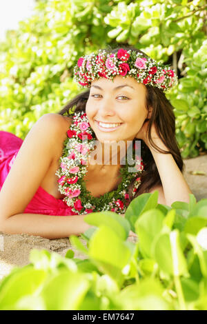 Hawaii, Local Girl Laying On Sand Wearing Flower Leis Surrounded By Bright Vegetation. Stock Photo