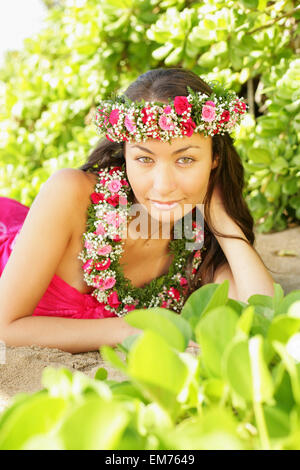 Hawaii, Local Girl Laying On Sand Wearing Flower Leis Surrounded By Bright Vegetation. Stock Photo