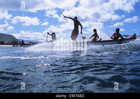 Hawaii, Oahu, Makaha, Man Standing Up In Outrigger Canoe While Surfing Wave, View From Side. No Model Release Stock Photo