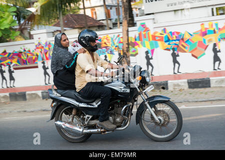 A man and woman riding on a motorbike through Fort Kochi, Kerala India Stock Photo