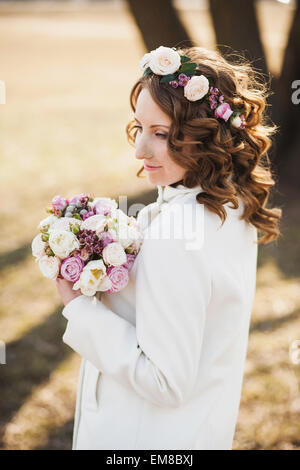 Beautiful young woman with delicate flowers in hair and bouquet of flowers in hands Stock Photo