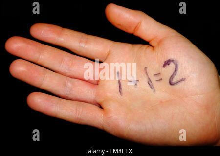 A simple maths sum written on the palm of a hand photographed against a black background. Stock Photo