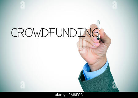 closeup of the hand of a young caucasian man in a grey suit writing the word crowdfunding in the foreground, slight vignette add Stock Photo