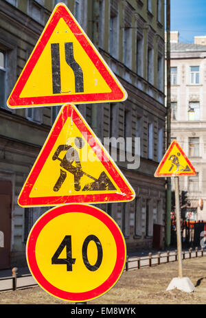 Bright red and yellow speed limit, under construction and narrowing of the road signs on one pole Stock Photo