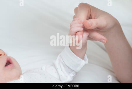 Baby girl holding mother's finger on bed Stock Photo