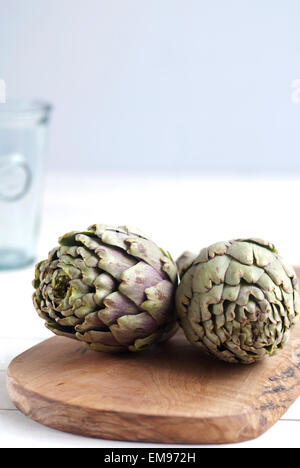 Still life food image of Globe Artichokes on an Olive wood chopping board against a neutral background with copy space. Stock Photo