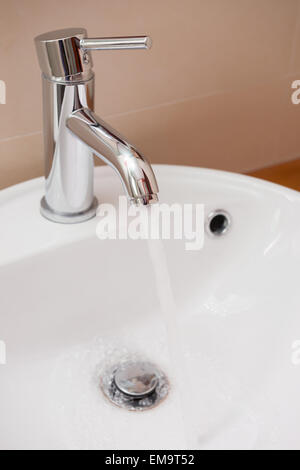water running out from stainless steel tap to a  washbasin in bathroom Stock Photo