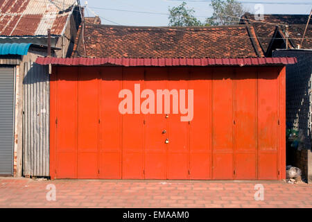 A bright red metal door stands padlocked on a city street in Kampong Cham, Cambodia. Stock Photo